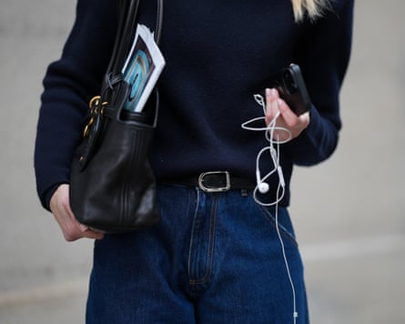 Street Style - Munich - February, 2026MUNICH, GERMANY - FEBRUARY 18: Mirja Klein is seen wearing a navy fine knit turtleneck sweater with long sleeves and a fitted silhouette from COS; dark wash baggy jeans with a relaxed oversized barrel fit and rolled-up legs from Dark Park; a slim black leather belt with silver buckle; a black „Aventure“ nappa leather bag with gold hardware, chain link details and a belted detail in the front closure from Miu Miu; holding an iPhone smartphone and wearing white wired earphones on February 18, 2026 in Munich, Germany. (Photo by Moritz Scholz/Getty Images)