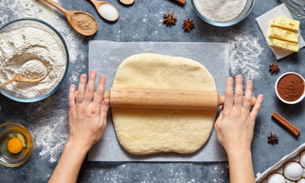 A person’s hands rolling out dough with a rolling pin