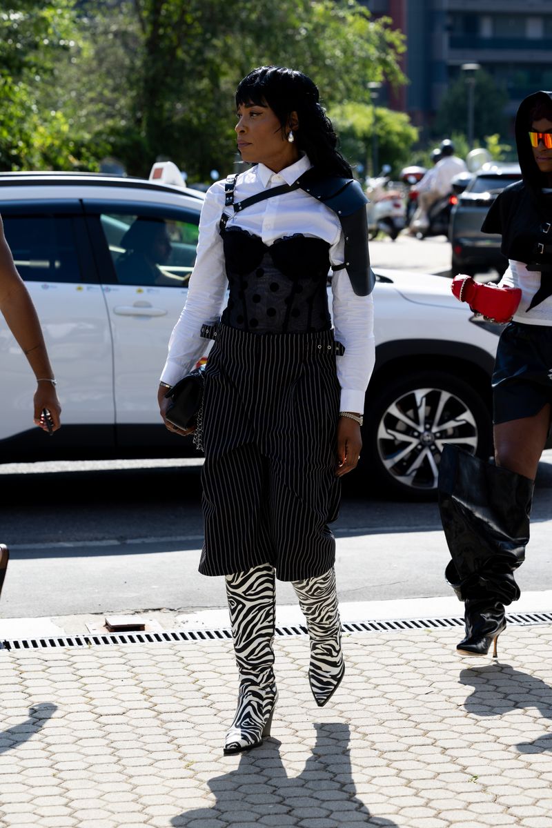 HRH Ifeanyichukwu of SHiiKANE wears black and white zebra printed knee high heeled boots, silver drop earrings, a white shirt.