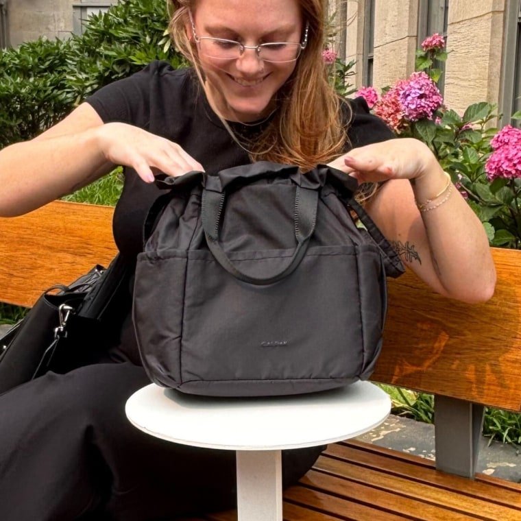 Woman sitting with Calpak Insulated Lunch Bag next to her.
