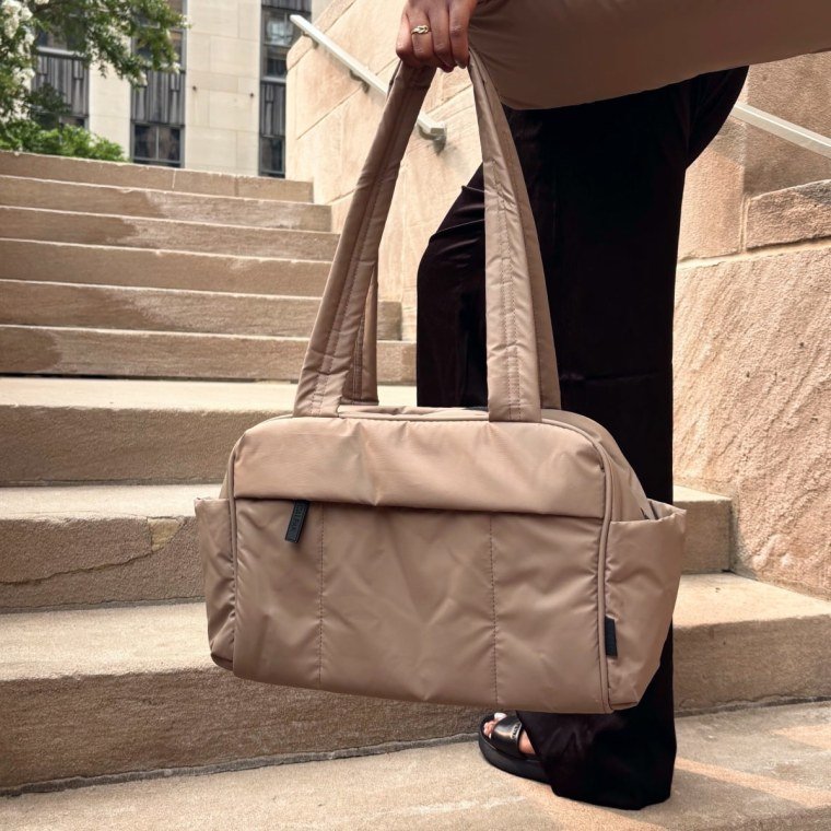 Woman holding a small Luka duffel in left hand on a staircase.