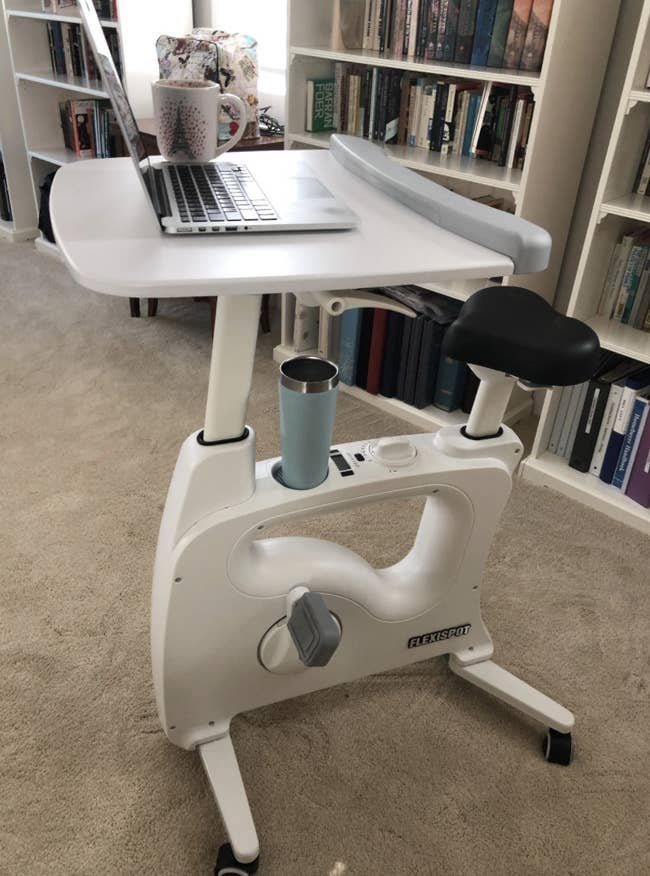 Reviewer image of white bike desk in a home with laptop propped on the tray and drink in the holder
