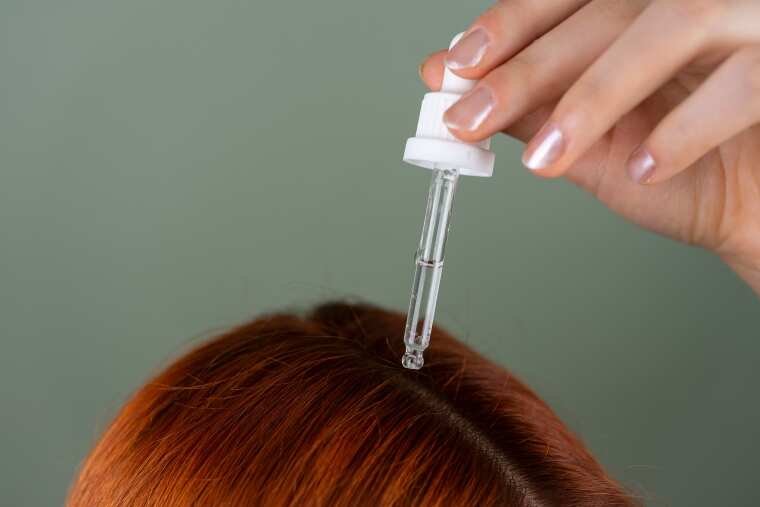 A woman applying serum on her scalp for hair care.