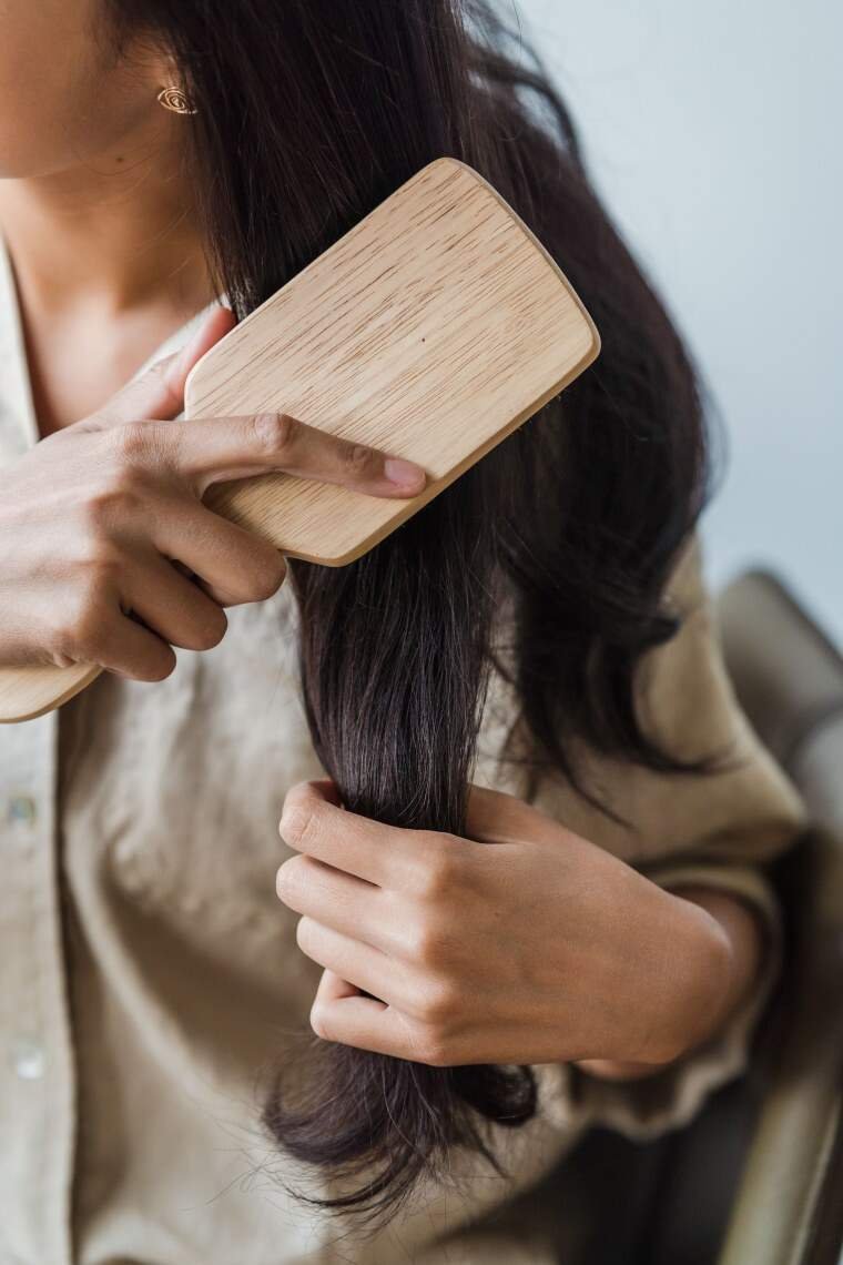 A woman combing her long hair with hair brush.