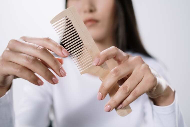A woman with a comb pondering over her hair condition.