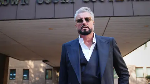 PA Media Fashion designer Catalin Botezatu - a middle aged man in a dark blue suit -leaving Southwark Crown Court