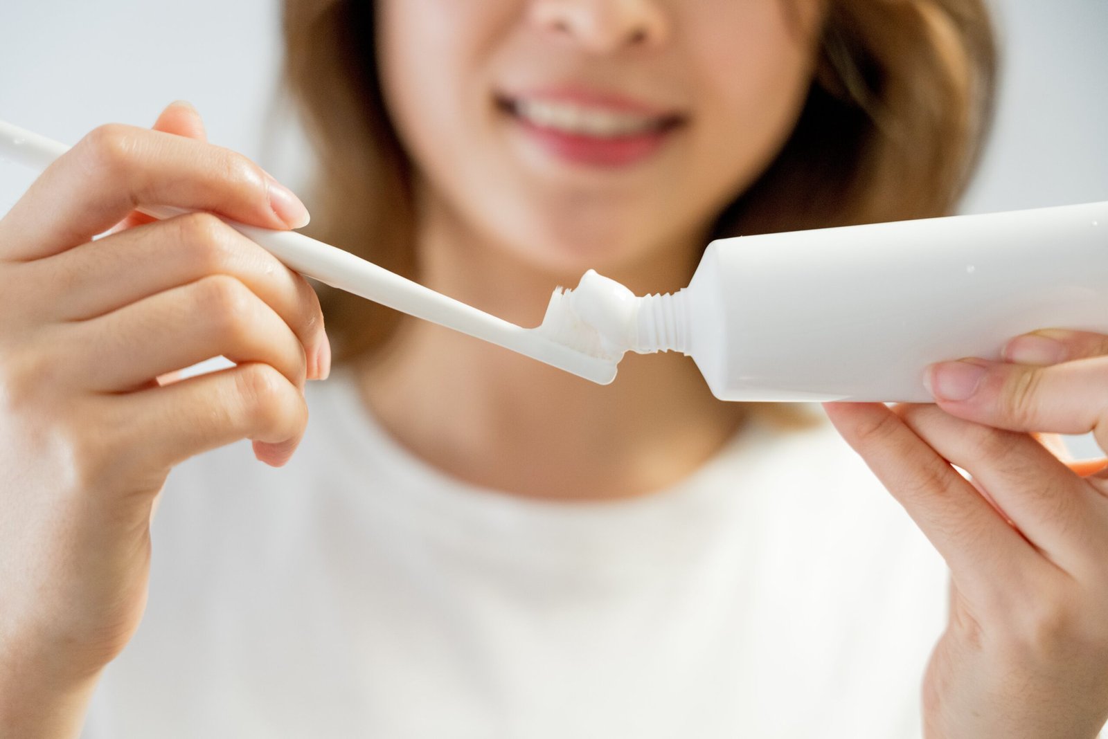 Person putting toothpaste on a toothbrush, smiling, focusing on dental hygiene