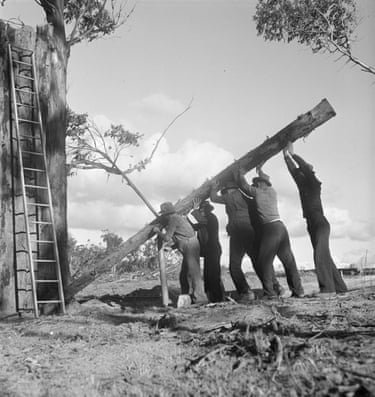 Black and white photograph of a group of men erecting a wooden pole