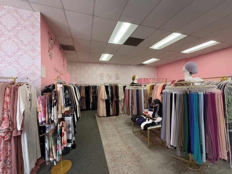 A clothing store with pink walls and racks of long gowns