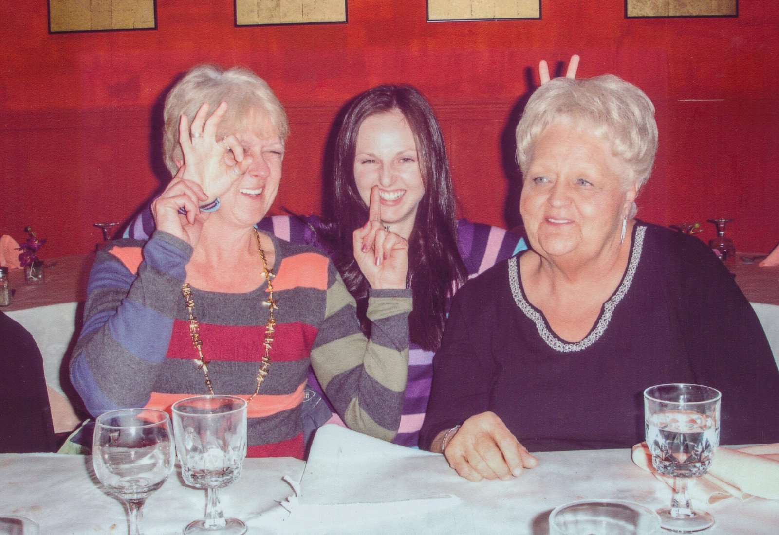 Three women at a table, smiling and playfully making gestures with their hands
