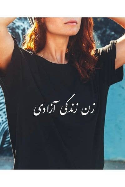 A woman with long hair wears a black t-shirt with white Arabic text.