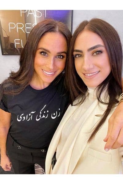 Two women smiling for the camera, one in a black t-shirt with Arabic text.